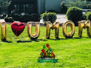 Outdoor yard balloon decor spelling out 'I Love You Mom' welcomes guests to a Mother's Day celebration, creating a festive and inviting atmosphere.