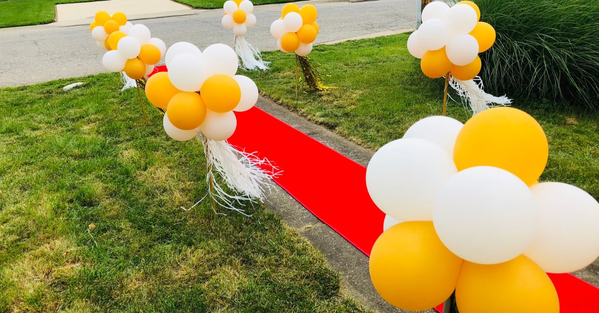 Red plush carpet lined with vibrant balloons for a stunning prom send-off decoration.